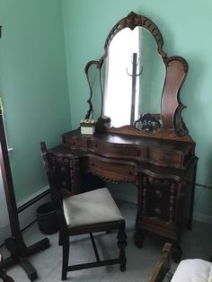 an antique vanity with mirror and stool in a room that has green walls, carpeted flooring and white trim