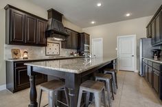 a kitchen with dark wood cabinets and marble counter tops, along with bar stools