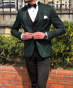 a man in a green tuxedo standing next to a brick wall and fence