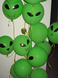 many green balloons with faces on them are hanging from the ceiling in front of a white wall