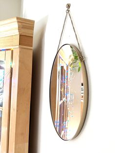 a mirror hanging from the side of a white wall next to a wooden cabinet and shelf