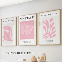 three framed art prints hang on the wall above a table with vases and books