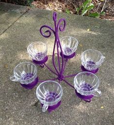 purple glass cups and saucers are arranged in the shape of a flower on concrete