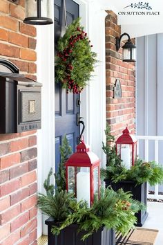 two red lanterns are on the front porch with christmas wreaths and greenery around them