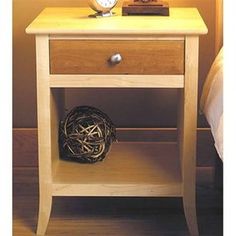 a night stand with a clock on it next to a bed