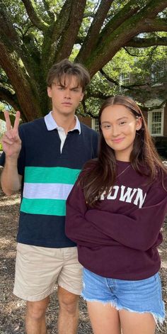 a man and woman standing next to each other in front of a tree with their fingers up