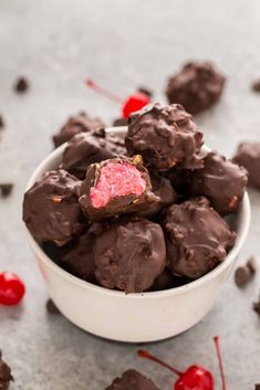 a white bowl filled with chocolate candy and cherries on top of a gray surface