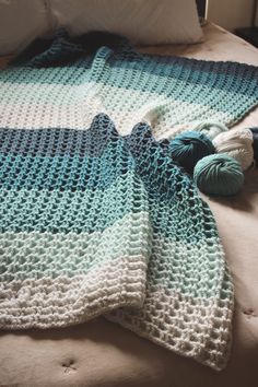 a crocheted blanket with balls of yarn on top of it, sitting on a bed