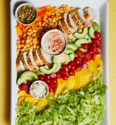 a platter filled with vegetables and meats on top of a yellow table cloth