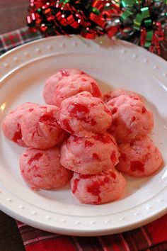 a white plate topped with red cookies on top of a table next to a christmas tree