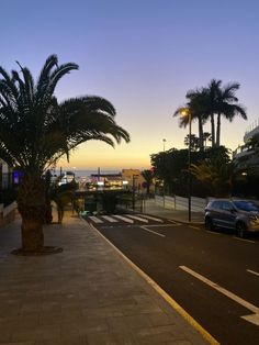 a car parked on the side of a road next to palm trees and buildings at sunset