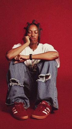 a person sitting on the ground with their legs crossed and wearing red shoes, against a red background