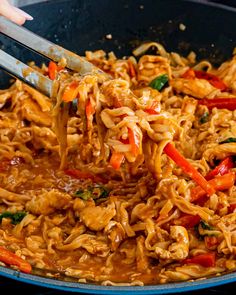 someone using tongs to stir noodles in a skillet with chicken and vegetables on the side