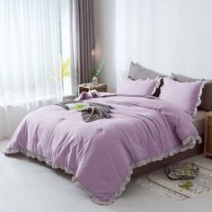 a bed with purple comforter and pillows in a white room next to a window