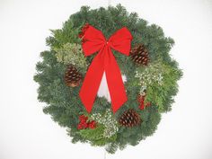 a christmas wreath with pine cones, holly and a red bow hanging on a white wall