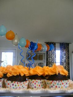 cupcakes with orange frosting and blue streamers are on a cake platter