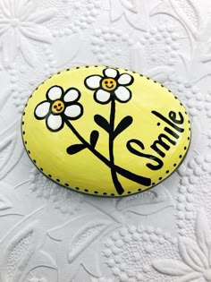 a yellow painted rock with white flowers and the words smile on it, sitting on a doily