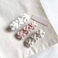 three crocheted flower clips sitting on top of a white cloth covered tablecloth