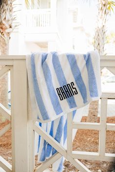 a blue and white striped towel hanging on a rail next to a house with palm trees in the background