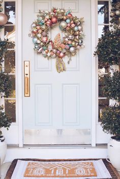 a christmas wreath on the front door of a house with ornaments hanging from it's side