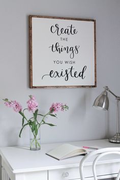 a white desk topped with a vase filled with pink flowers next to a sign that says create the things you wish excited