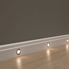 three lights are on the side of a wall near a wood floor and white trim