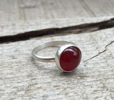 A lovely blood red round carnelian has been set in sterling silver with a handmade ring band from sterling silver half dome wire. The carnelian is 10mm in size and has a deep red color to it. A dark patina or oxidized finish has been applied to darken the silver which enhances the bright blood red of the carnelian. Made to order! Choose your size and finish. Ruby Ring With Polished Finish And Round Band, Red Carnelian Ring With Polished Finish, Red Carnelian Rings With Polished Finish, Red Polished Carnelian Rings, Red Carnelian Cabochon Ruby Ring, Carnelian Cabochon Ruby Ring, Red Carnelian Oval Cabochon Ruby Ring, Red Cabochon Ruby Ring, Carnelian Ruby Ring With Oval Cabochon For Gift