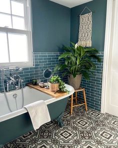 a bathroom with blue tiles and a green plant in the bathtub next to it