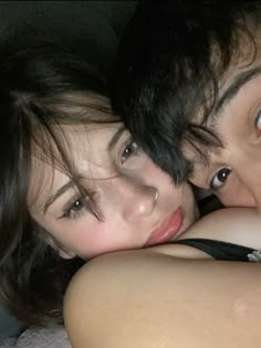 two people laying on top of each other with their arms around one another and looking at the camera