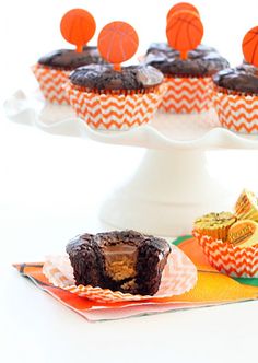 cupcakes with basketball decorations on them sitting in front of an orange and white cake stand