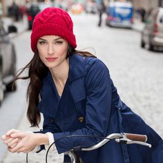 a woman wearing a red hat riding a bike down a street next to parked cars