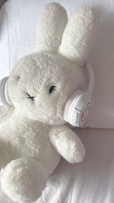 a white stuffed animal laying on top of a bed with headphones in its ears