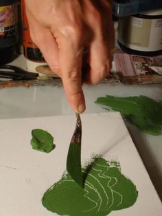 a person is using a brush to paint green leaves on a piece of white paper