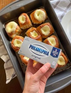 a person holding up a box of pastries in front of a plate of food