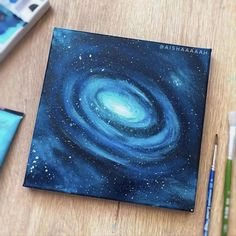 a painting of a spiral galaxy on a wooden table next to markers and pencils