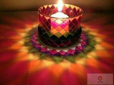 a lit candle sitting on top of a colorful table cloth with the light shining through it