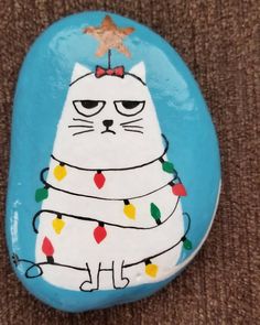 a painted rock with a cat wearing a christmas sweater on it's face and lights around its neck