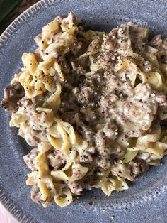 a blue plate topped with pasta covered in meat and gravy on top of a wooden table