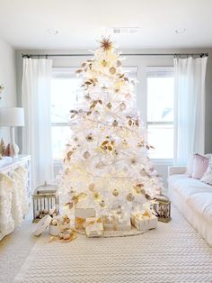 a white christmas tree in the corner of a living room with a woman sitting next to it