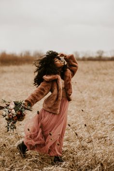 a woman in a dress and fur coat walking through a field