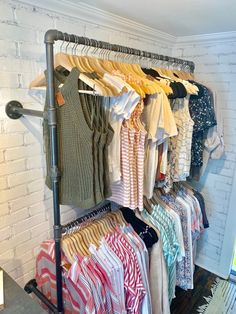 a rack full of clothes in front of a white brick wall