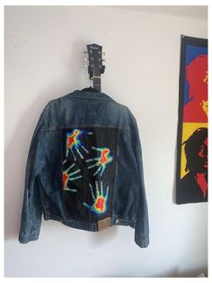 a jacket hanging on the wall next to a painting and guitar pick up rack with two guitars