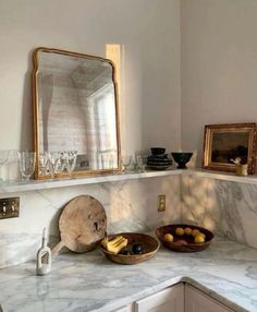 a white marble counter top sitting under a mirror next to a bowl filled with fruit