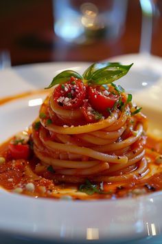 a white plate topped with pasta covered in tomato sauce and garnished with basil