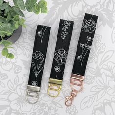 three black and white flowered belts with gold buckles next to a potted plant