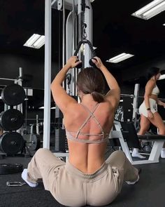 a woman sitting on the ground in front of a gym machine with her back to the camera