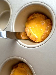 two mini muffins with cheese in them being held by a spoon and placed inside the muffin cups