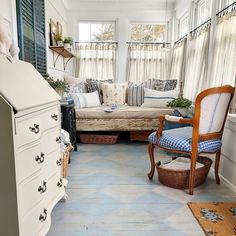 a living room filled with furniture next to a window covered in white curtains and blue checkered pillows