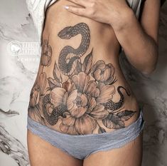 a woman with a snake and flowers tattoo on her stomach is looking at her cell phone