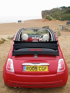 a red car parked on top of a sandy beach next to the ocean with its roof down